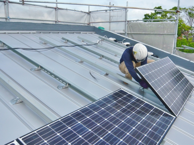 ２階建て住宅の屋根に太陽光パネルの設置工事を行っています。